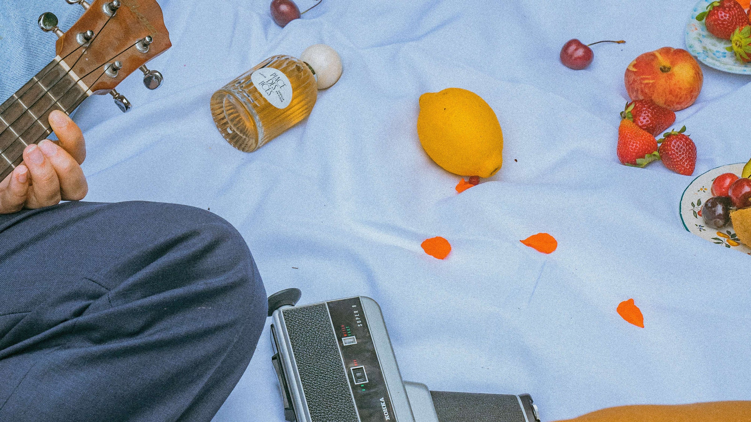 A bottle of 'Vanille en Fleur' rests on a soft white blanket as a group of friends picnic.