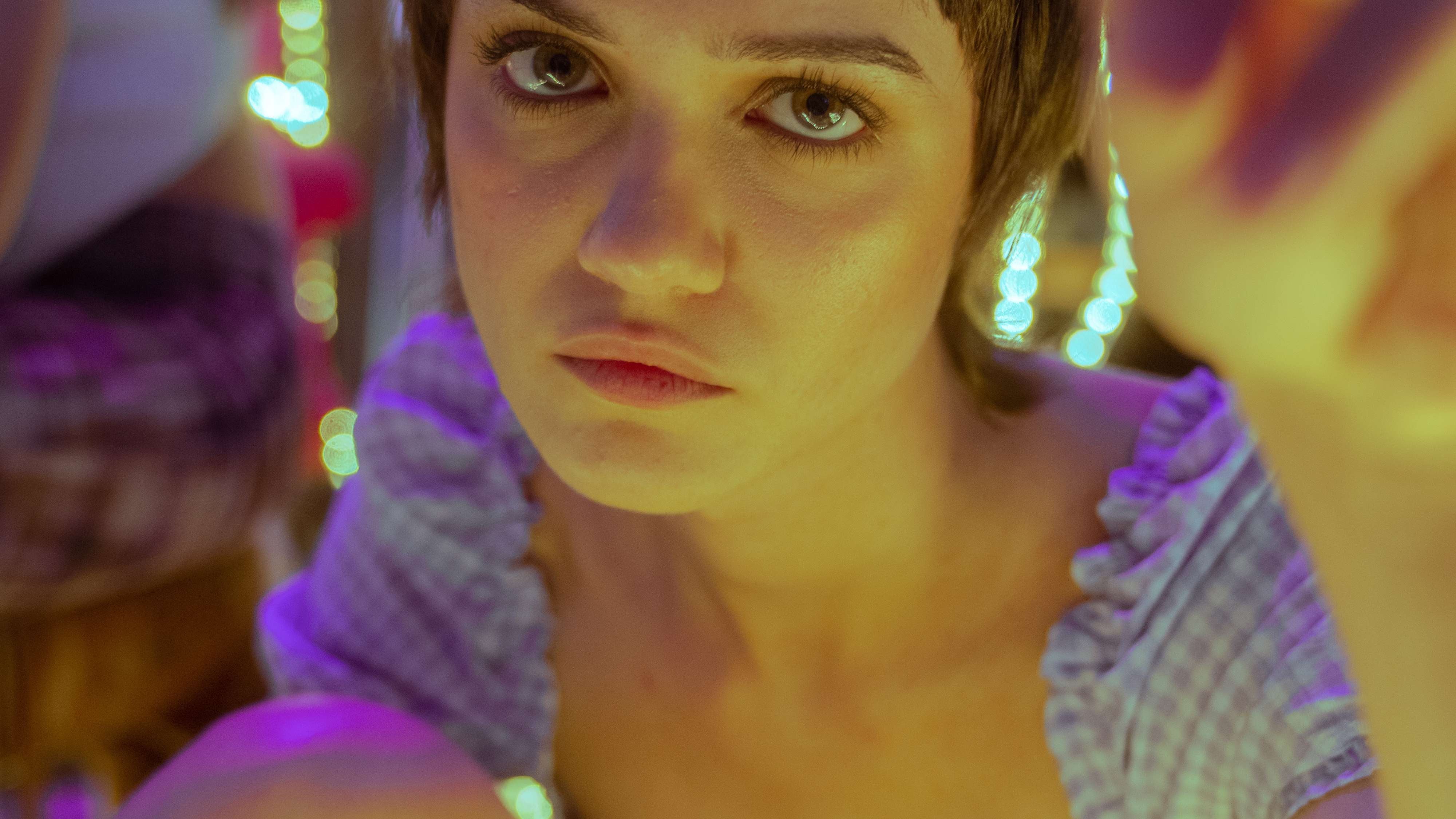 A women surrounded by fluorescent lights stars directly at the camera.