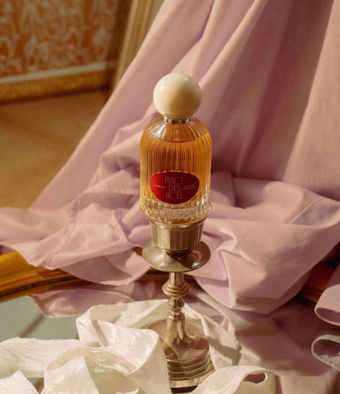 A bottle of Safran Gourmand sits a top a silver candle holder, surrounded by linens.